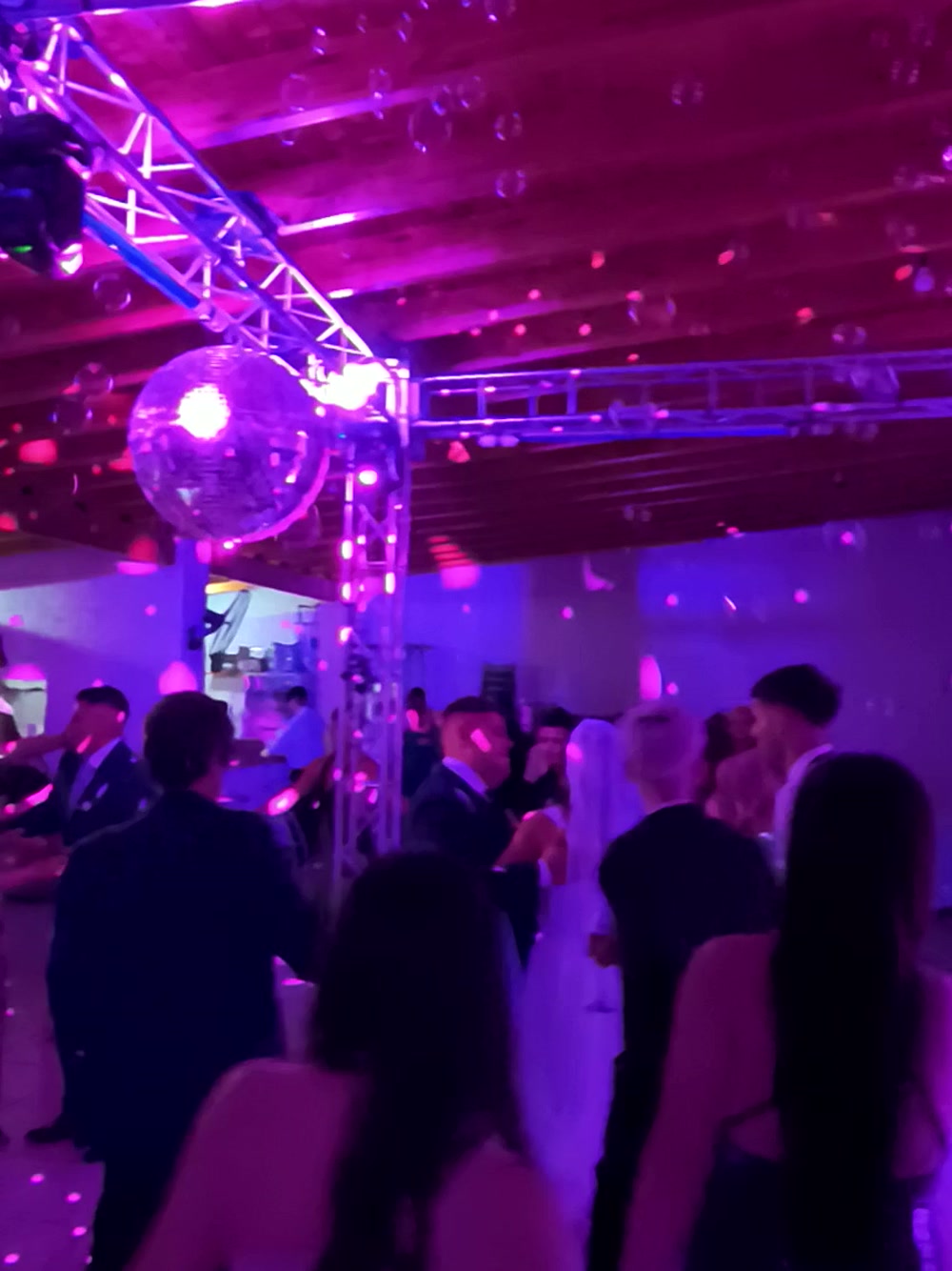 Pista llena de invitados bailando bajo la bola de espejos y las estructuras de luz en un casamiento en Mendoza