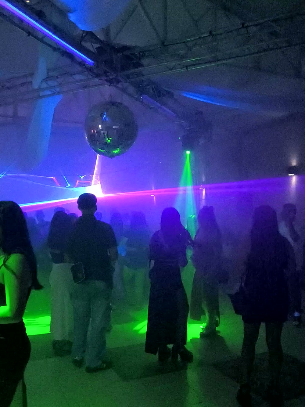 Pista llena de invitados bailando bajo lásers, bola de espejos y estructuras de luz